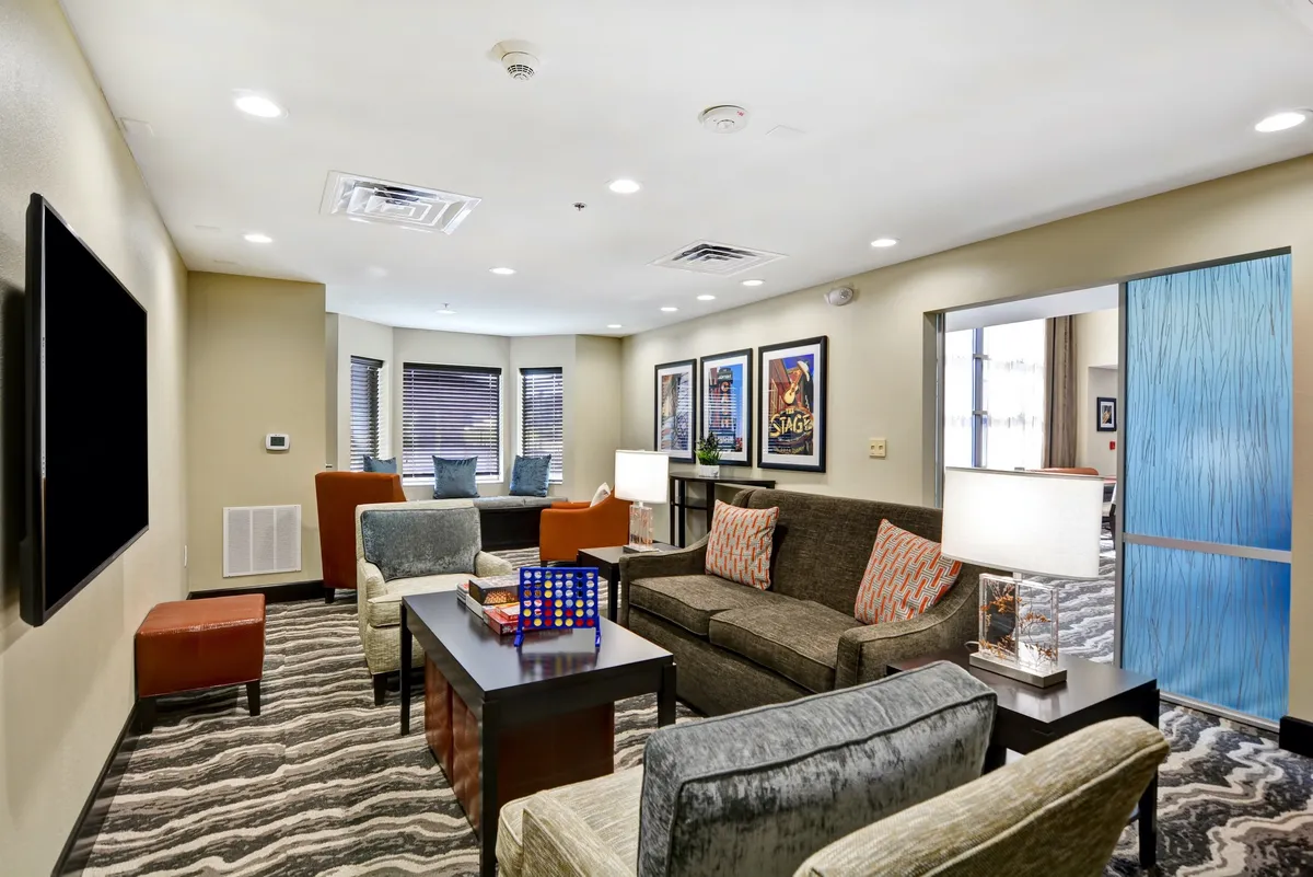 A welcoming living room with a comfortable seating area featuring a plush sofa, colorful artwork on the walls, a modern coffee table, and varied furniture textures. The arrangement is casual and inviting, perfect for relaxing, watching TV, or socializing.