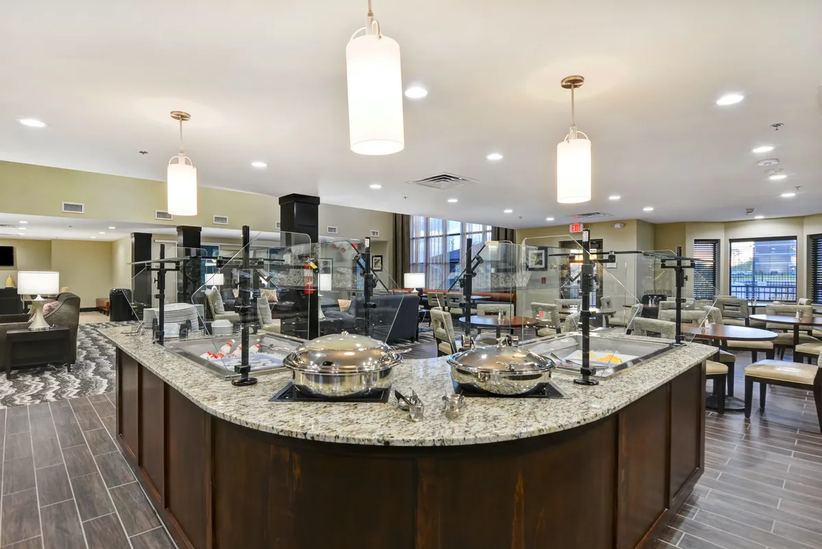 A communal granite countertop holds serving dishes under warm lighting fixtures, hinting at gatherings or casual dining. The scene evokes a sense of community, where guests can share meals or snacks together, with an inviting and communal mood.