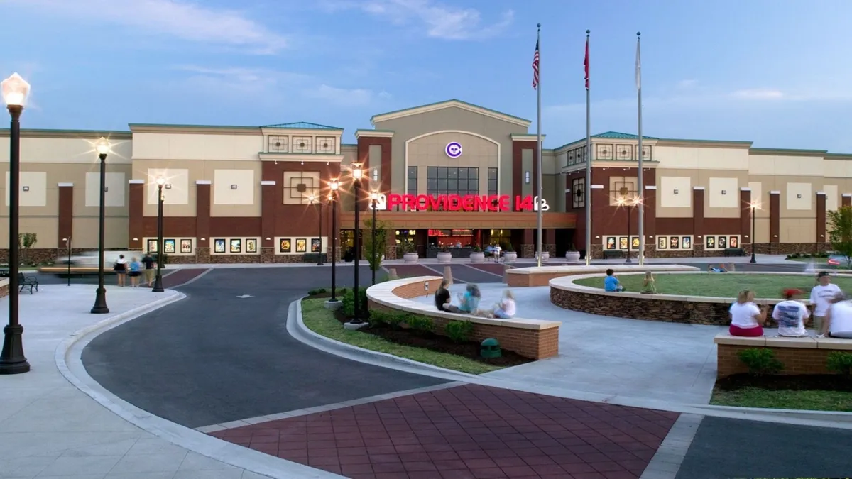 The welcoming facade of a local theater, illuminated at dusk, with its prominent entrance and inviting outdoor seating area. The environment suggests a social, casual spot for guests to enjoy movies, mingle, or simply soak up the neighborhood vibe.