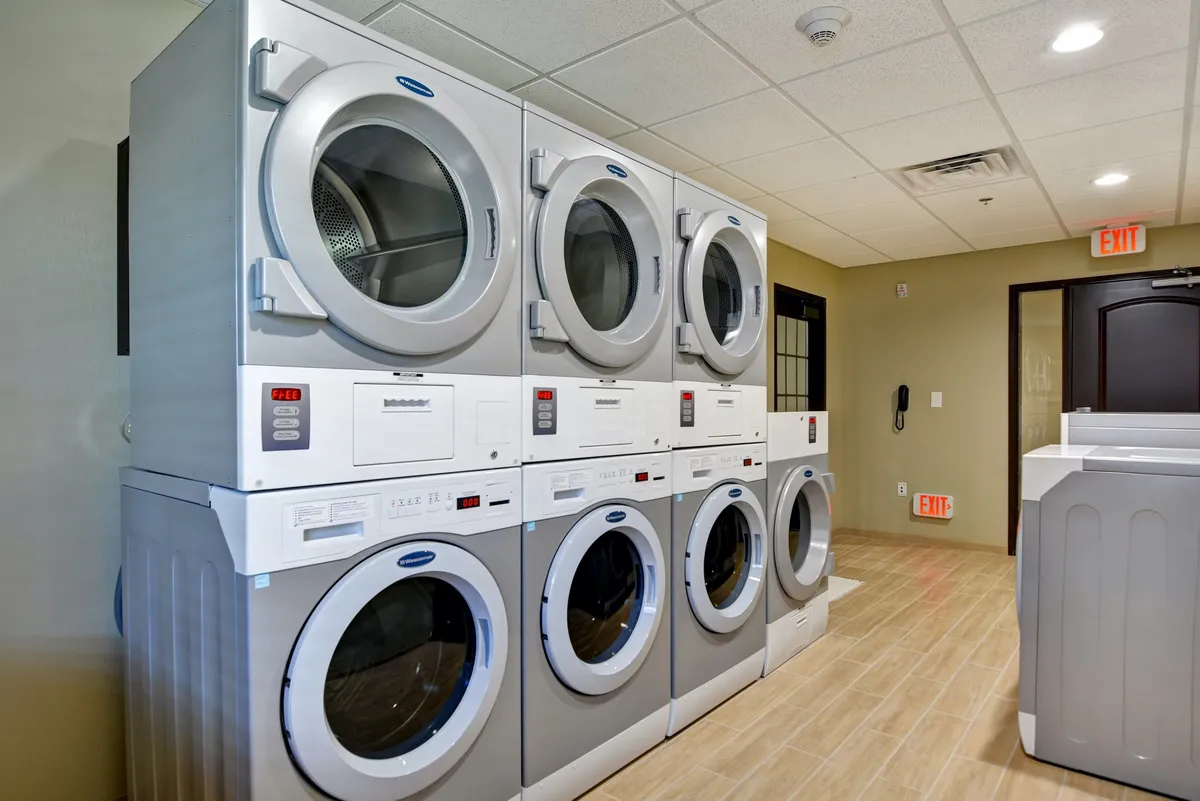 The image displays a laundry area with stacked washing machines, dryers, and a designated folding area. The setting is practical and clean, suggesting convenience and ease for guests staying in the condo.