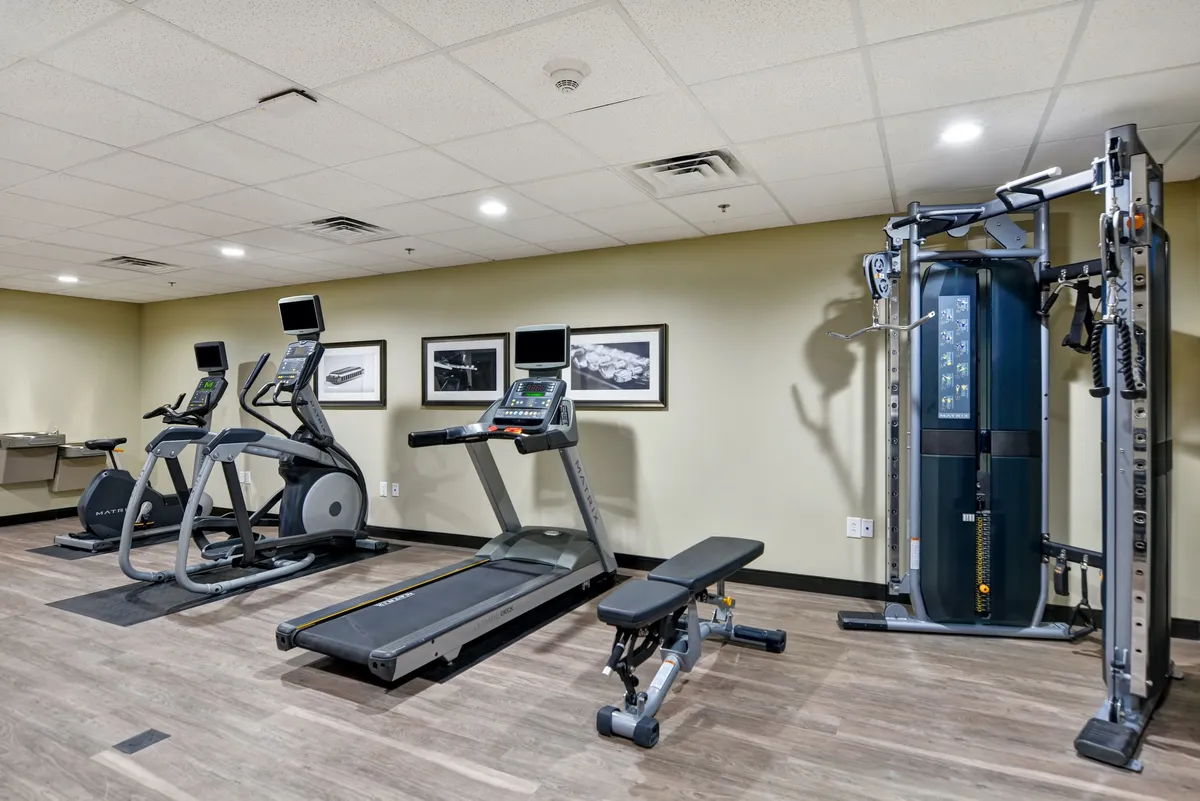 A modern 24-hour fitness center outfitted with treadmills, elliptical machines, a weight bench, and a multi-gym setup. The space is well-lit, energetic, and designed for both cardio and strength training, suitable for guests maintaining their exercise routines while traveling.