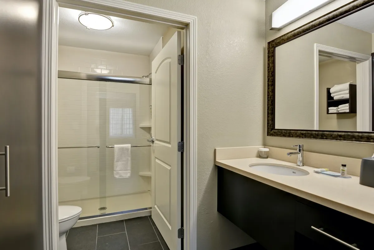 This image showcases a modern bathroom interior, featuring a vanity with a sleek sink, a spacious shower area, and a well-lit mirror. The bathroom appears inviting and refreshing, with clean lines and thoughtful design details that convey comfort and luxury.