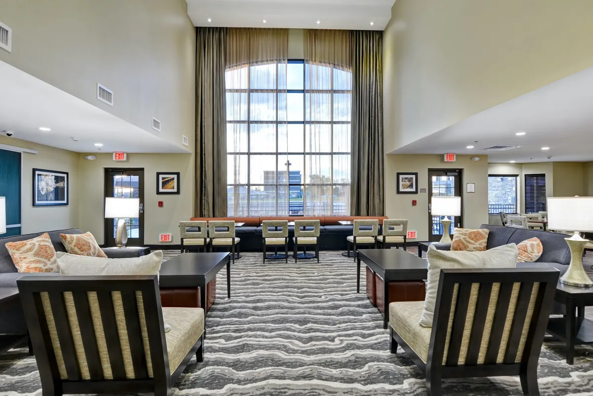 A modern living space illuminated by a large window with elegant drapery, featuring a stylish coffee table, decorative pillows, and a cozy seating area. The setup is suited for both casual gatherings and quiet moments, emphasizing comfort and contemporary style.