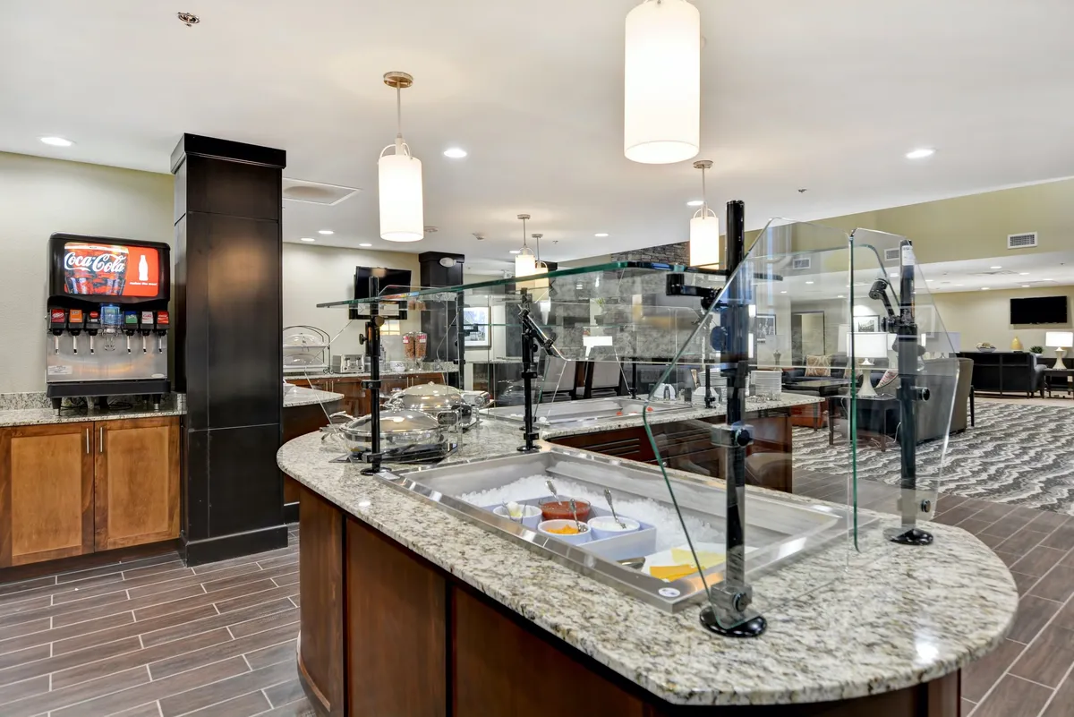 An inviting breakfast area with a granite countertop buffet featuring a variety of food and beverages, complemented by stylish lighting fixtures and a casual, welcoming seating arrangement. The space is bright, clean, and conducive to social gatherings or a relaxing start to the day.